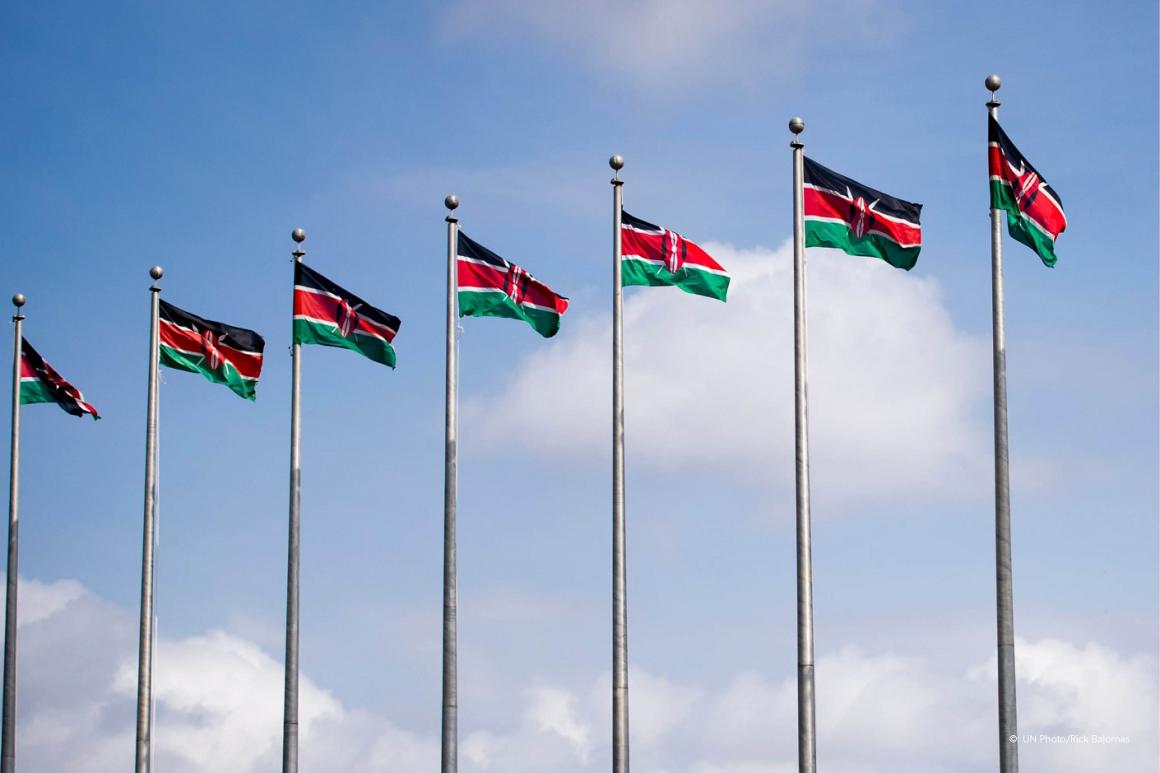Rangée de sept drapeaux kenyans flottant au sommet de mâts sur fond de ciel bleu parsemé de quelques nuages 