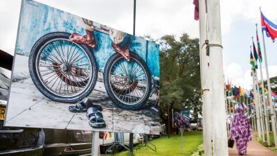 A large billboard displaying bicycle wheels and sandals, with international flags and a person in the background.