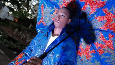 A person holding a colorful, patterned umbrella looks thoughtfully into the distance, wearing a matching jacket.
