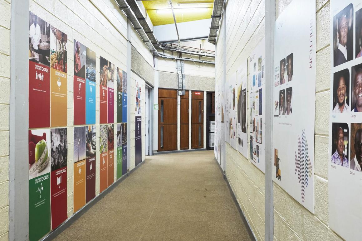 A corridor with several photographs of staff and some of the UN SDGs (Sustainable Development Goals) exhibited by the Publishing Services Section of UNON
