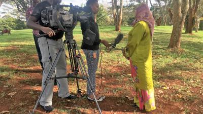 A camera crew, with a videographer and sound person, interviews Amina J. Mohammed outdoors.