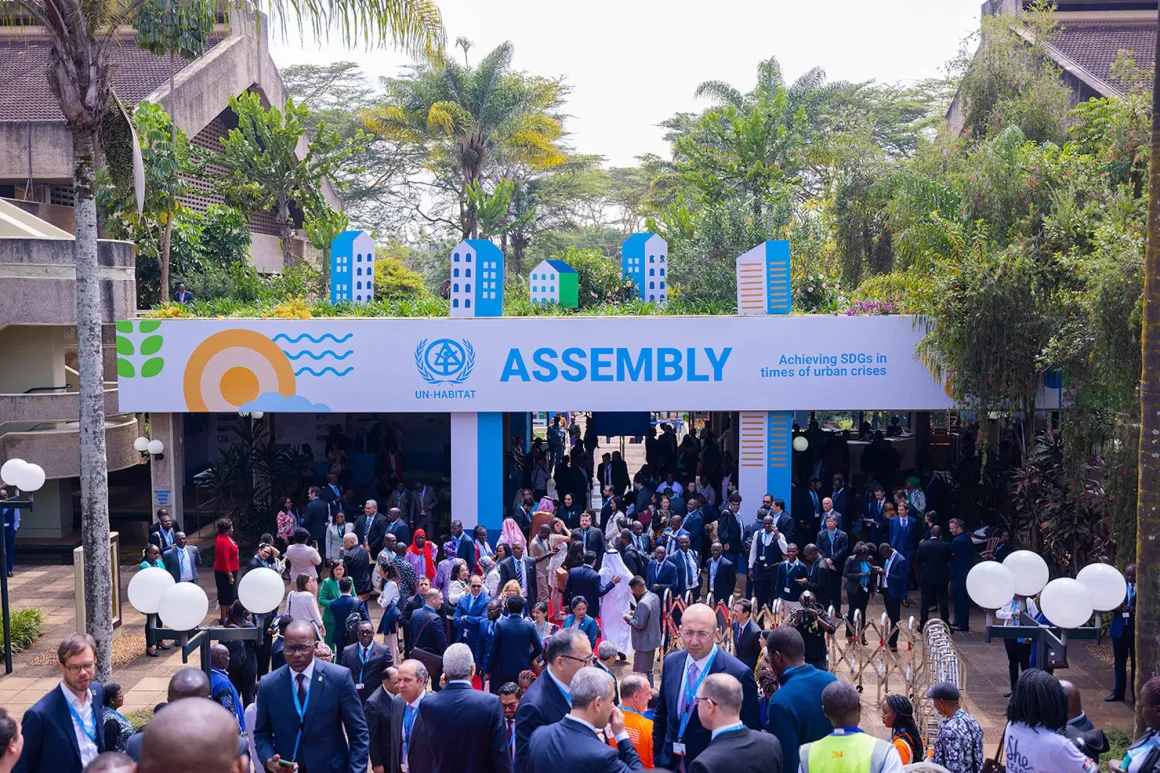 People gathered below a sign for the UN-Habitat Assembly.